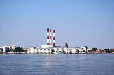 Buildings by sea against clear blue sky