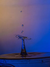 Close-up of drop falling on water against blue background