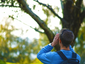 Rear view of man with backpack looking at tree using binoculars