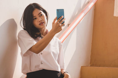 Young woman using mobile phone against wall