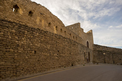 Low angle view of stone wall against cloudy sky