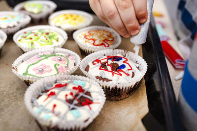 A child squeezes colored frosting from a tube onto chocolate brown cupcakes covered  decorations.