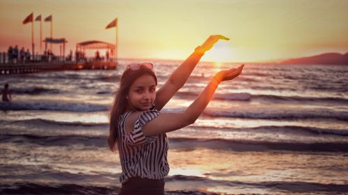 Optical illusion of woman holding sun while standing at beach against sky during sunset