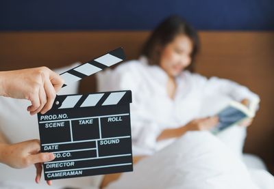 Cropped hand holding film slate against woman sitting on bed