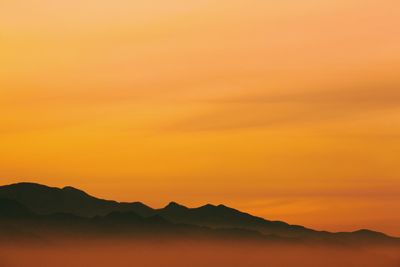 Scenic view of silhouette mountains against orange sky