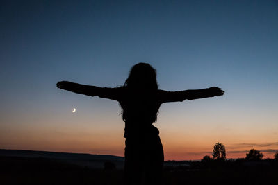 Silhouette woman with arms outstretched standing at beach against sky during sunset