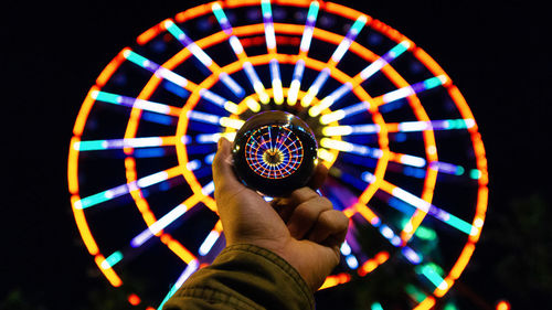 Cropped hand of man holding crystal ball against illuminated ferris wheel