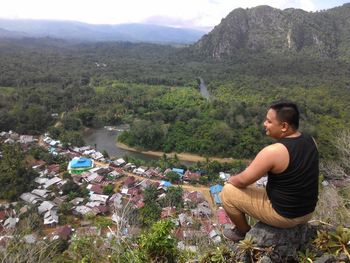 Young man sitting on land against mountains