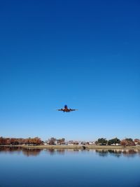 Airplane flying over lake against clear blue sky