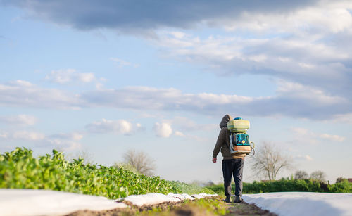 A farmer with a poison sprayer walks across the plantation field. protection of cultivated plants 