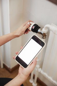 Woman holding phone and using radiator thermostat