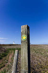 Road sign on wooden post in field against clear blue sky