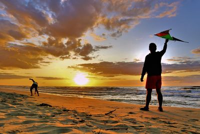 Silhouette people on beach against sky during sunset