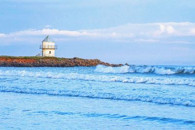 Lighthouse on beach by sea against sky