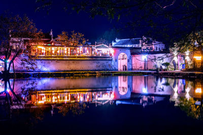 Illuminated buildings by lake at night