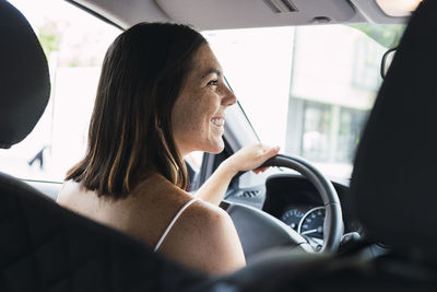 Happy young woman sitting on driver's seat in car