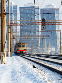 An electric train moves on rails against the backdrop of a cityscape in a winter haze vertical image