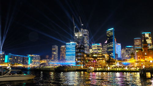 Illuminated buildings by river against sky in city at night