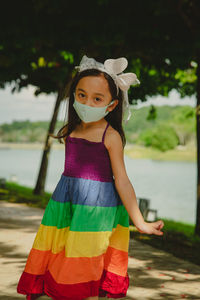Little girl wearing face mask with rainbow dress enjoying outdoor in the park. new normal.
