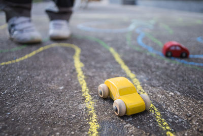 Low section of child standing by toy cars on road