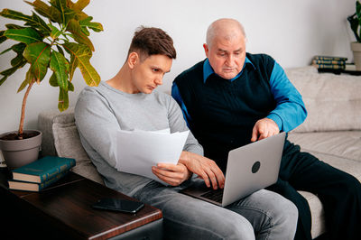 Grandfather and man using laptop together in living room at home