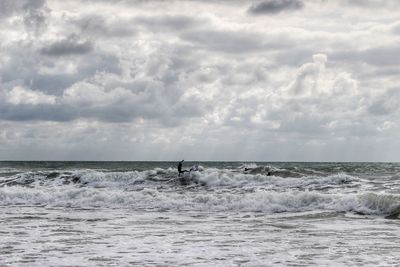 Man surfing on sea against cloudy sky