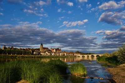 Arch bridge over river by buildings against sky