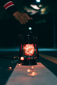 Cropped hand holding illuminated lantern on road at night