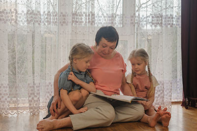 Full length of grandmother with granddaughters reading book at home