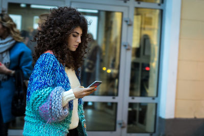 Young woman using smart phone while standing by laptop