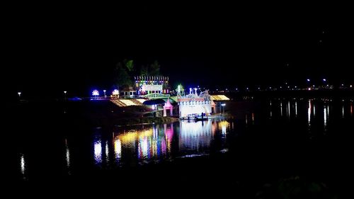 Illuminated buildings by river against sky at night