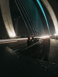 People on illuminated bridge against sky in city at night