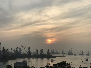 Cranes at commercial dock against sky during sunset