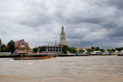 Boat on river by buildings against cloudy sky