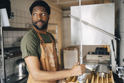 Male baker looking away while washing utensils in commercial kitchen