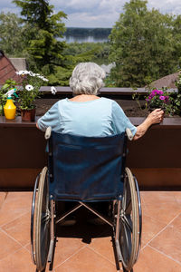 Back view of an old woman in wheelchair planting flowers in small terrace garden