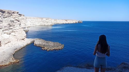 Rear view of woman looking at sea shore against clear sky