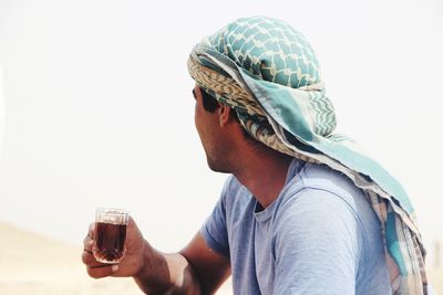 Side view of man wearing headscarf while having drink at desert