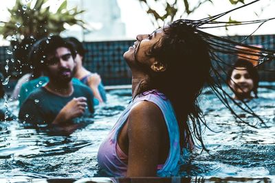 Friends looking at woman tossing hair in swimming pool