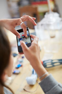 Cropped image of young female technician touching mobile screen while photographing model on table at workshop