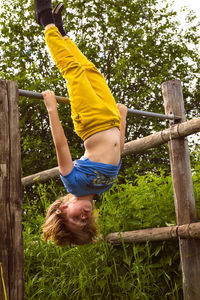 A boy in yellow pants makes a stand on the horizontal bar upside down. sports activities in nature. 