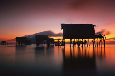 Silhouette built structure by sea against orange sky