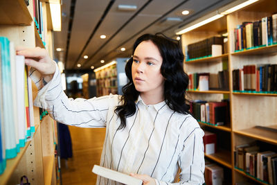 Young female student searching book in university library