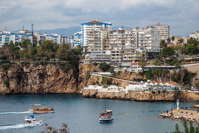 Boats sailing in river by cityscape against sky