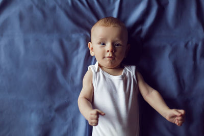 Baby boy blonde in white bodysuit lying on the bed