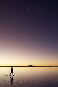 Silhouette person walking on wet shore against clear purple sky