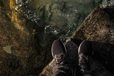 Low section of person standing on retaining wall by lake