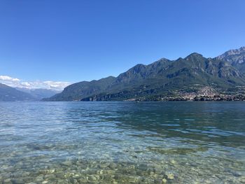 Scenic view of lake by mountains against clear blue sky