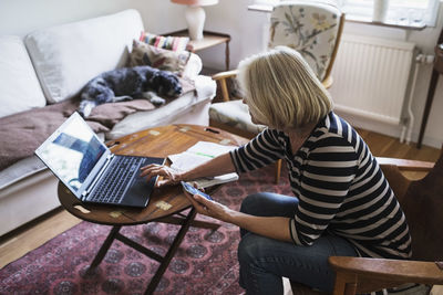 Side view of senior woman using laptop at home while dog relaxing on sofa