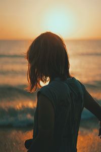 Rear view of woman in sea against sky during sunset